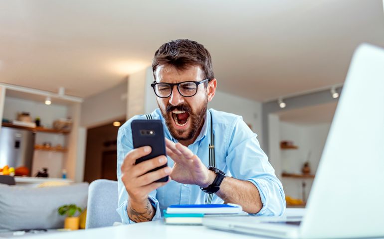 Angry man talking on phone disputing over computer laptop problem