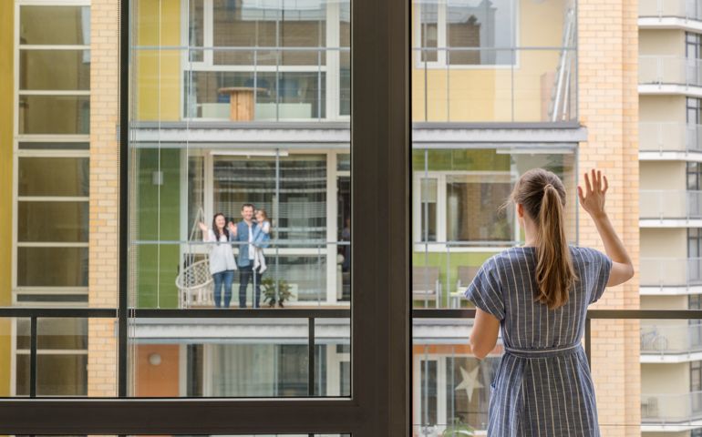 Back view of woman standing on balcony waving to her neighbours