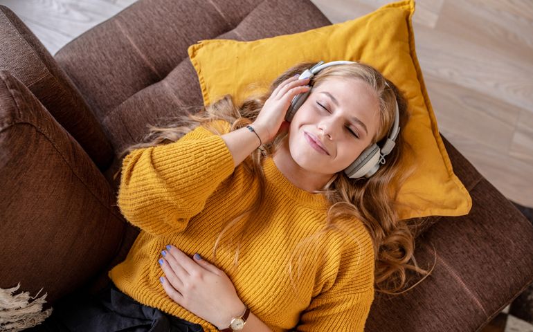 Photo of young woman with headphones laying on the couch and smiling