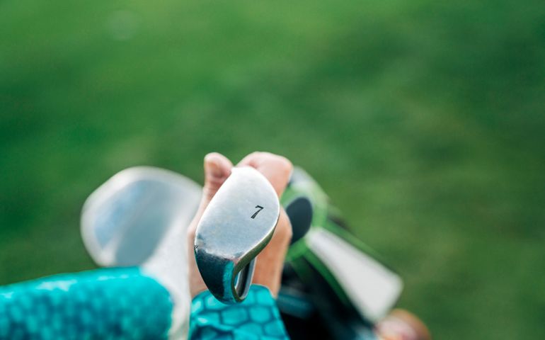 Hand of active female golfer holding club with number 7. High angle view of senior athlete at turf