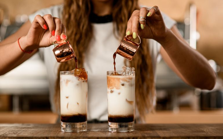 process of making macchiato with syrup. Woman pours coffee from cups into glasses