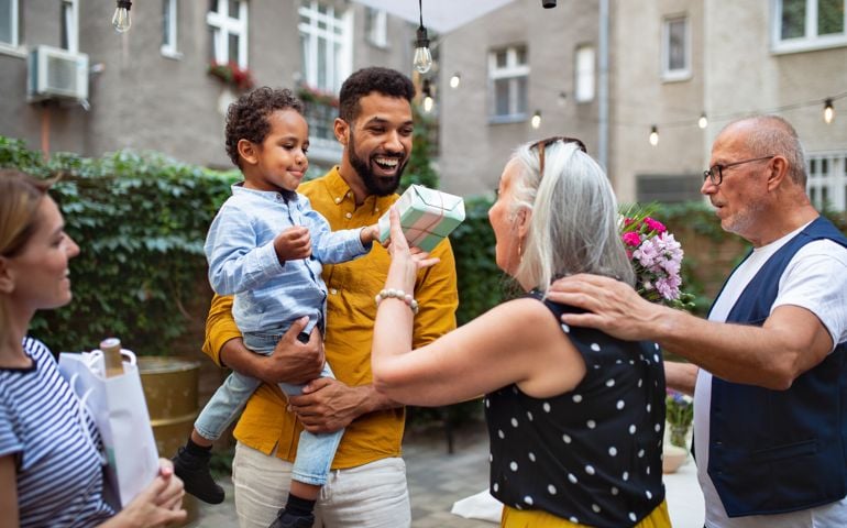Cheerful senior woman getting birthday gift from her small grandson outdoors in front or back yard.