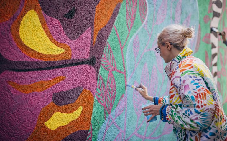 One woman, young female street artist painting on a building wall outdoors.