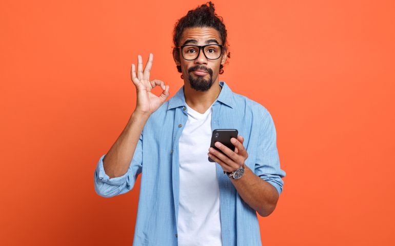 Isolated studio shot of young african american man showing ok sign with mobile phone in hand