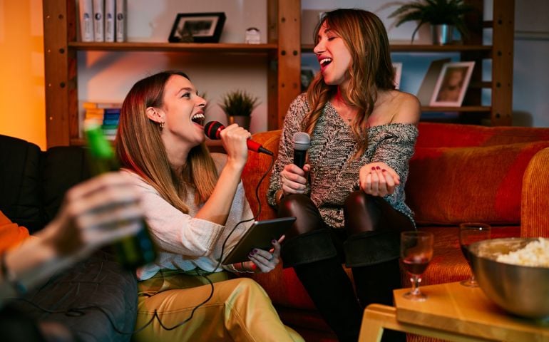 Happy girls sitting at home and singing a duet. Karaoke night.