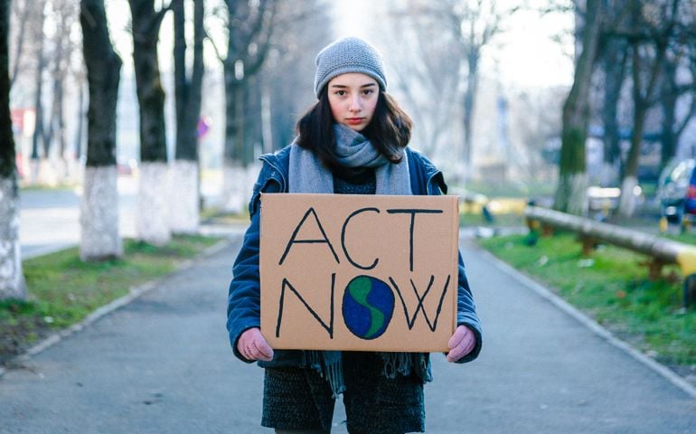 Portrait of a young teenage girl activist holding a sign protesting against climate change and global warming.
