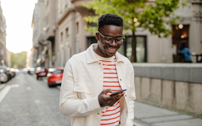 The portrait of an man is on the street, he is walking and using a mobile phone on the go