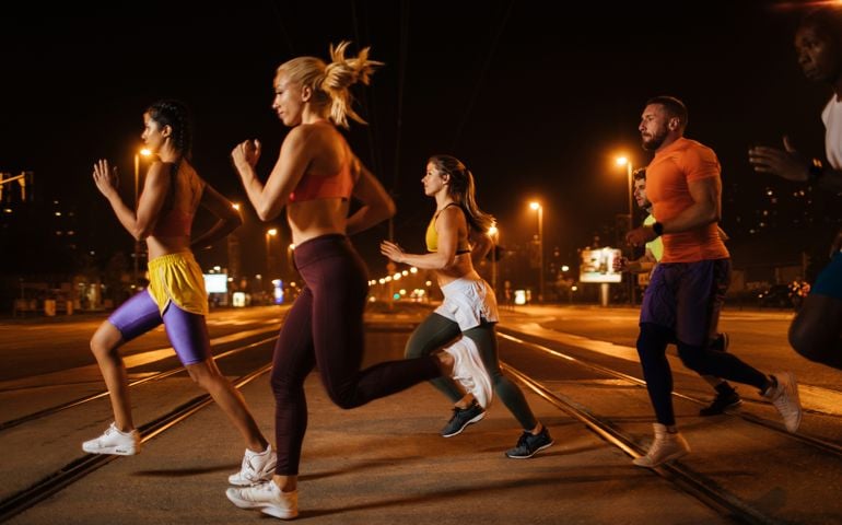 Team of athletic young people running through the city streets at night