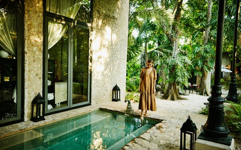 Wide shot of smiling woman standing pool and putting foot in water at luxury tropical spa