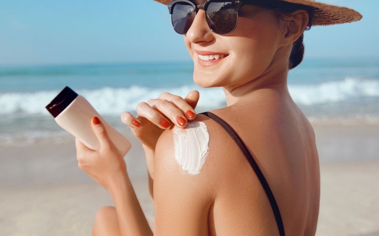 Girl Using Sunscreen to Skin. Beautiful Woman in Bikini Applying Sun Cream on Tanned Shoulde