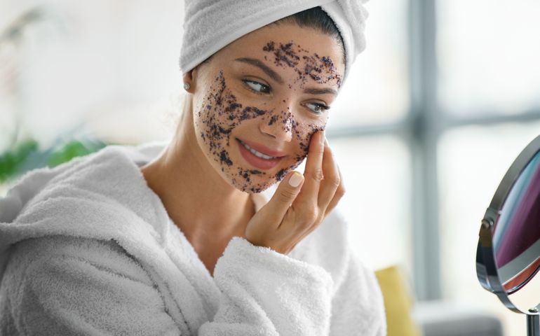 Young woman applying face scrub product on her face while looking at mirror