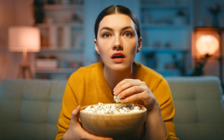 Young woman watching TV, movies with popcorn. Girl spending time at home.