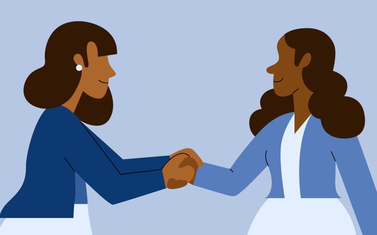 Two businesswomen shake hands while connecting and networking while smiling dressed in business casual attire