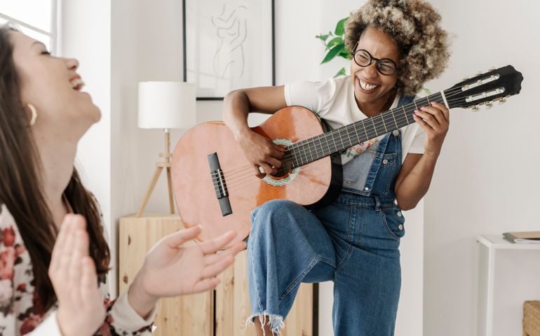 Young female couple playing guitar and laughing in the bedroom.