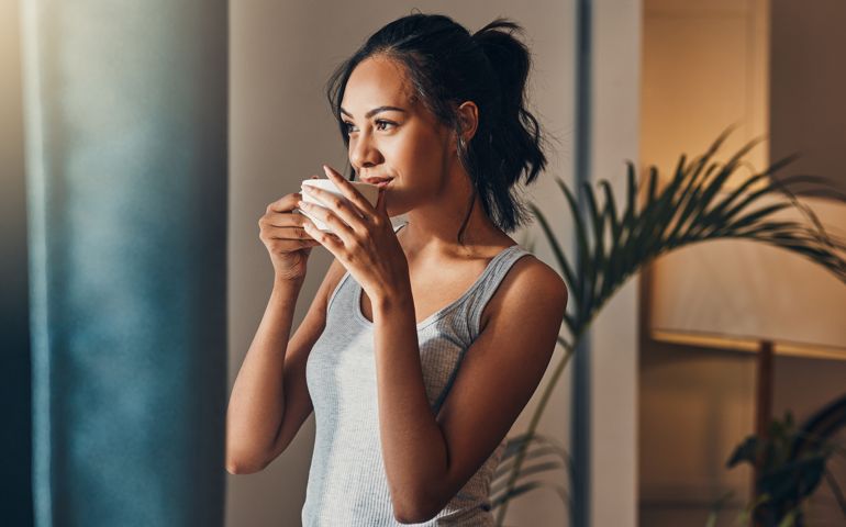 A beautiful young woman enjoying a warm cup of coffee for breakfast