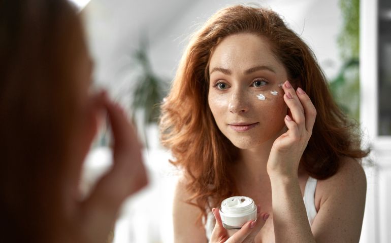 Young redhead woman smiling and applying face cream