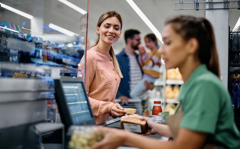 Happy woman paying for groceries at checkout while buying with her family in supermarket.
