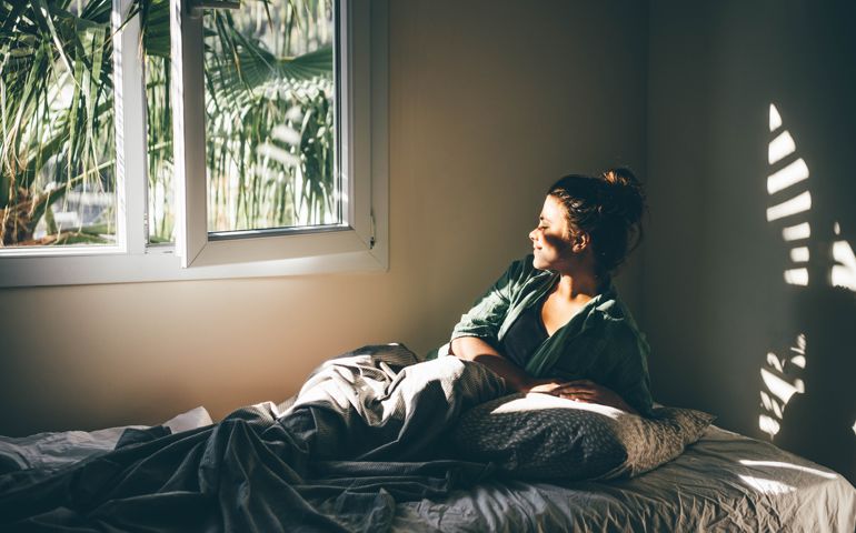 Woman waking up and relaxing near window at home.
