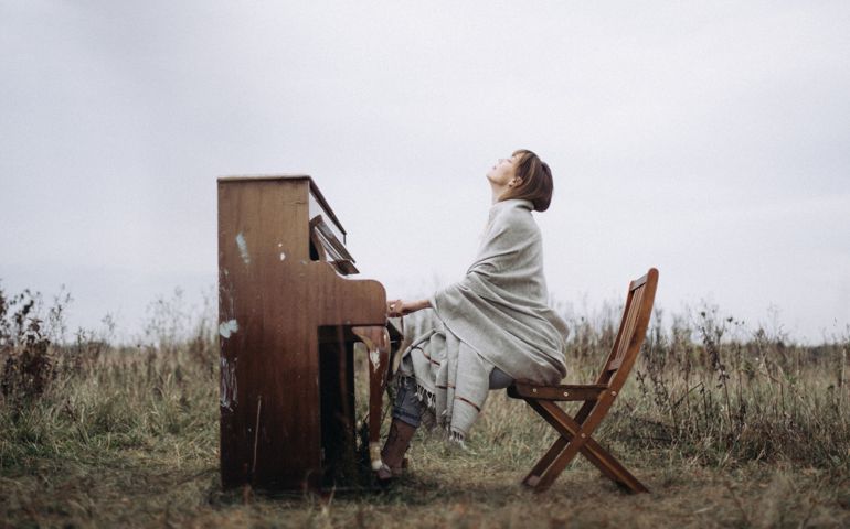 A beautiful woman is playing the piano with pleasure in a field in autumn