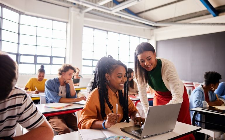 Smiling teacher talking with a student using a laptop during a classroom lesson