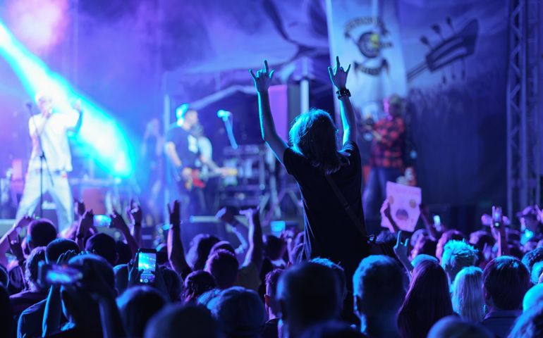 Youth is excited during street rock concert. They dance. Bright blue neon lighting. Night life of the big city. Back view
