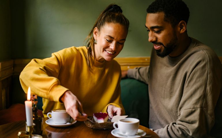 Female enjoying raspberry dessert while boyfriend watches