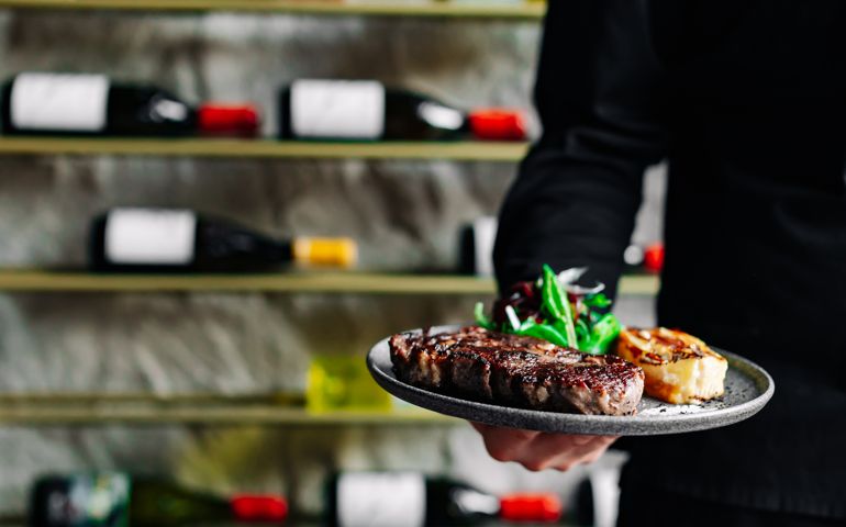 Young handsome chef in black uniform hold in his hands ready beef steak ribeye meat