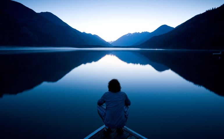 Person sitting quietly on the edge of a dock watching the sunset
