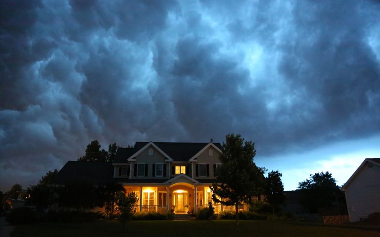 A well appointed house is lit up while a large thunderstorm moves in overhead. Ample copy space above.