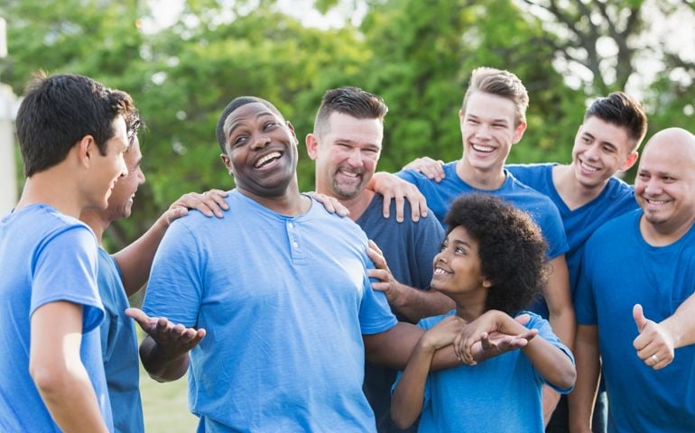 A group of men and sons standing together outdoors in the park wearing blue shirts