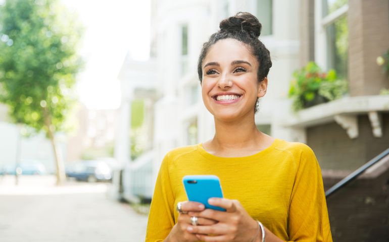 Happy woman with smart phone on street.