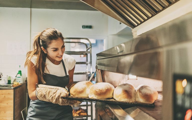 Young woman baker taking out the hot bread from the oven.