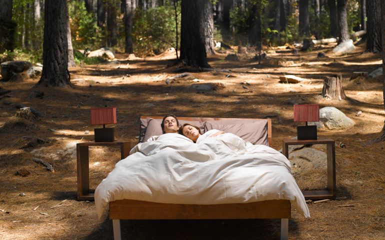 A couple sleeping in a bed outdoors in the woods