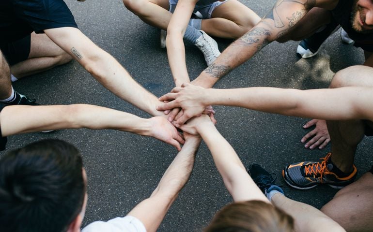 Group Of Athletes Bring Hands Together In Unity Before Friendly Outdoor Basketball Match