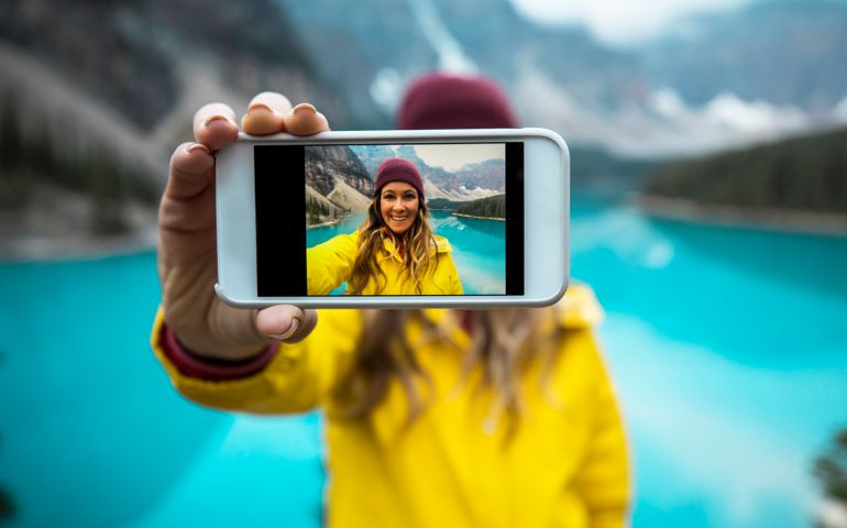 A young woman in a yellow jacket taking a cell phone selfie