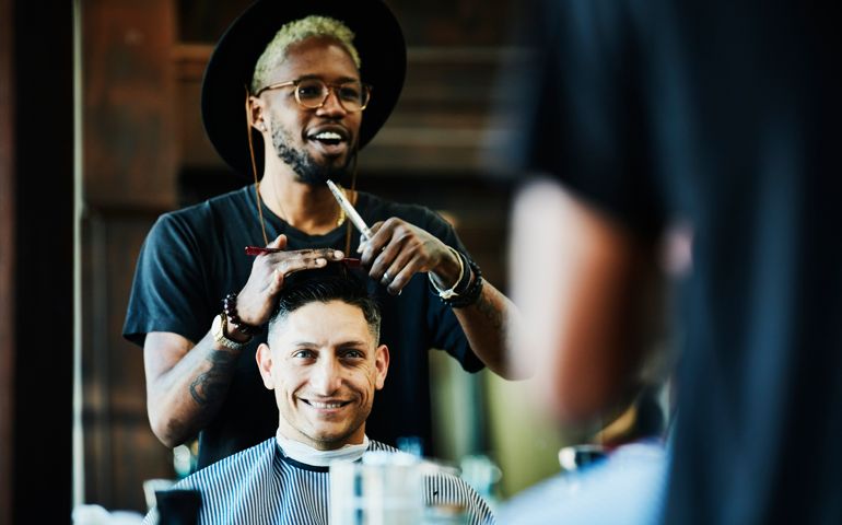 Smiling barber in discussion with client while cutting hair in barber shop