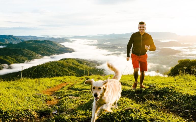 Young Man And Dog Running On Mountain Against Cloudy Sky