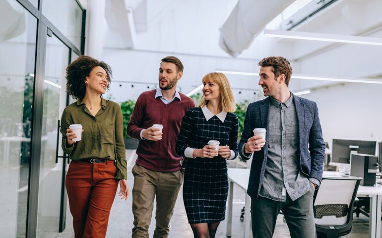 Group of coworkers walking through a corridor in an office, holding paper cups