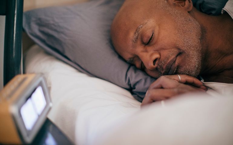 Retired senior man sleeping on bed by alarm clock at home