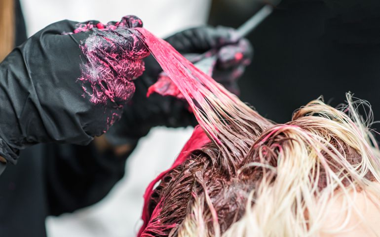Closeup of the hands of a hairdresser in black gloves dye the hair strand of the client's girl red.
