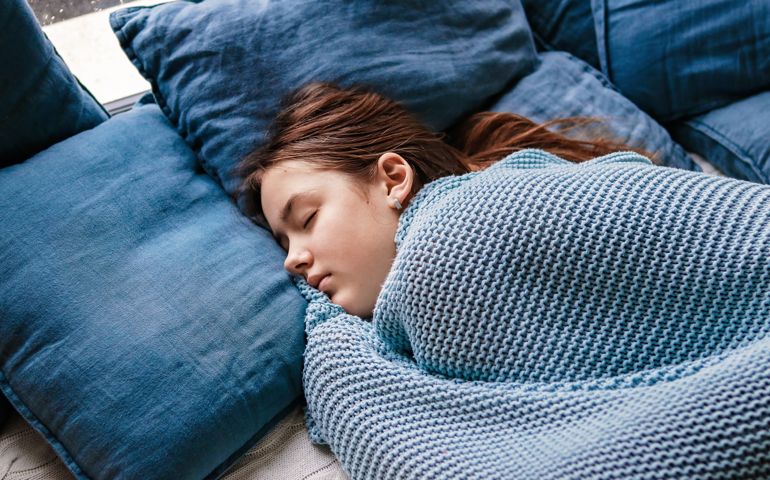 Young teenager girl sleeping snuggled in warm knitted blue blanket. Seasonal melancholy, apathy and winter blues.