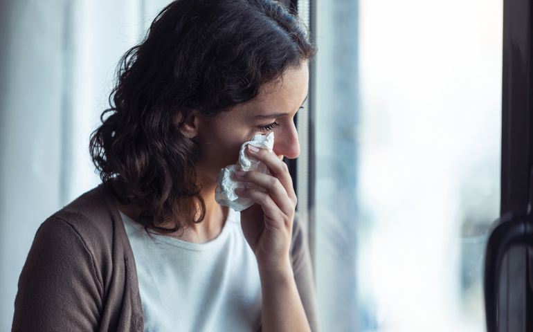 Sad young woman crying while looking through the window at home.