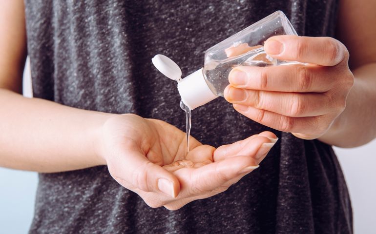 Close up view of woman person using small portable antibacterial hand sanitizer on hands.