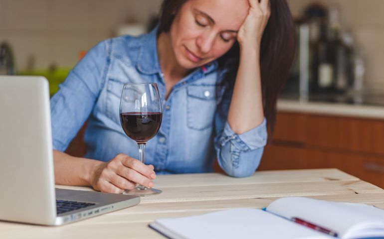 Depressed woman drinking red wine at home.