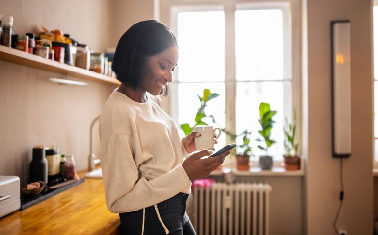 Woman having coffee and texting on her phone at home
