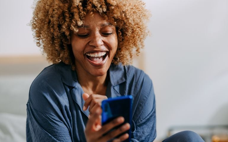 Smiling Woman Using Mobile Phone in the Bedroom