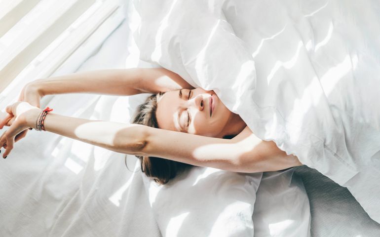 Woman sleeping under duvet at the sunny morning, top view.