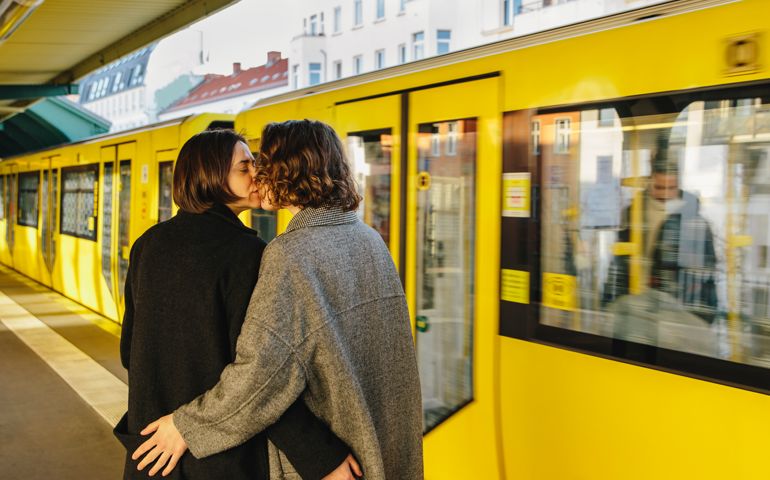 couple kissing while standing by yellow train at railroad station