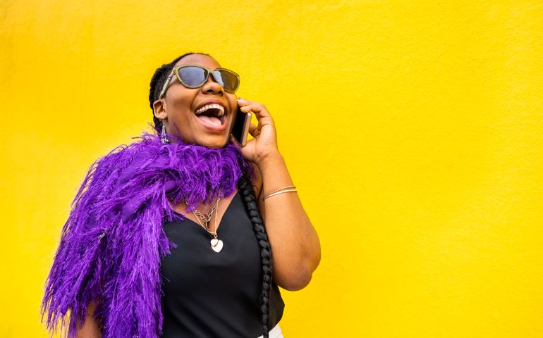 Stylish young woman talking on a phone and laughing by a yellow wall outdoors