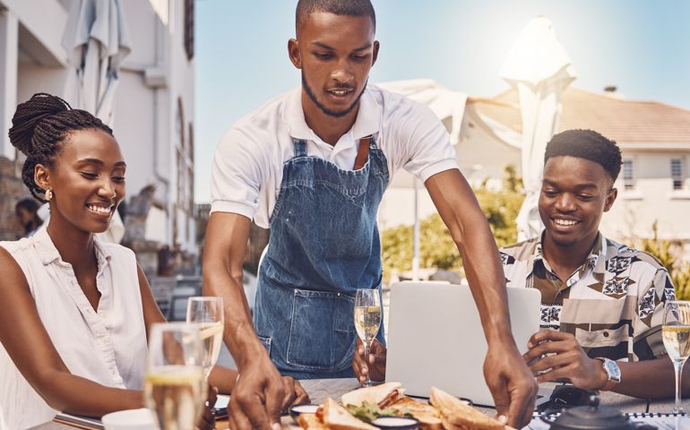 Waiter serving food to couple at a restaurant, worker giving service and food on table at a cafe in summer. Happy man and woman eating lunch at a shop, happy with server and date at coffee shop